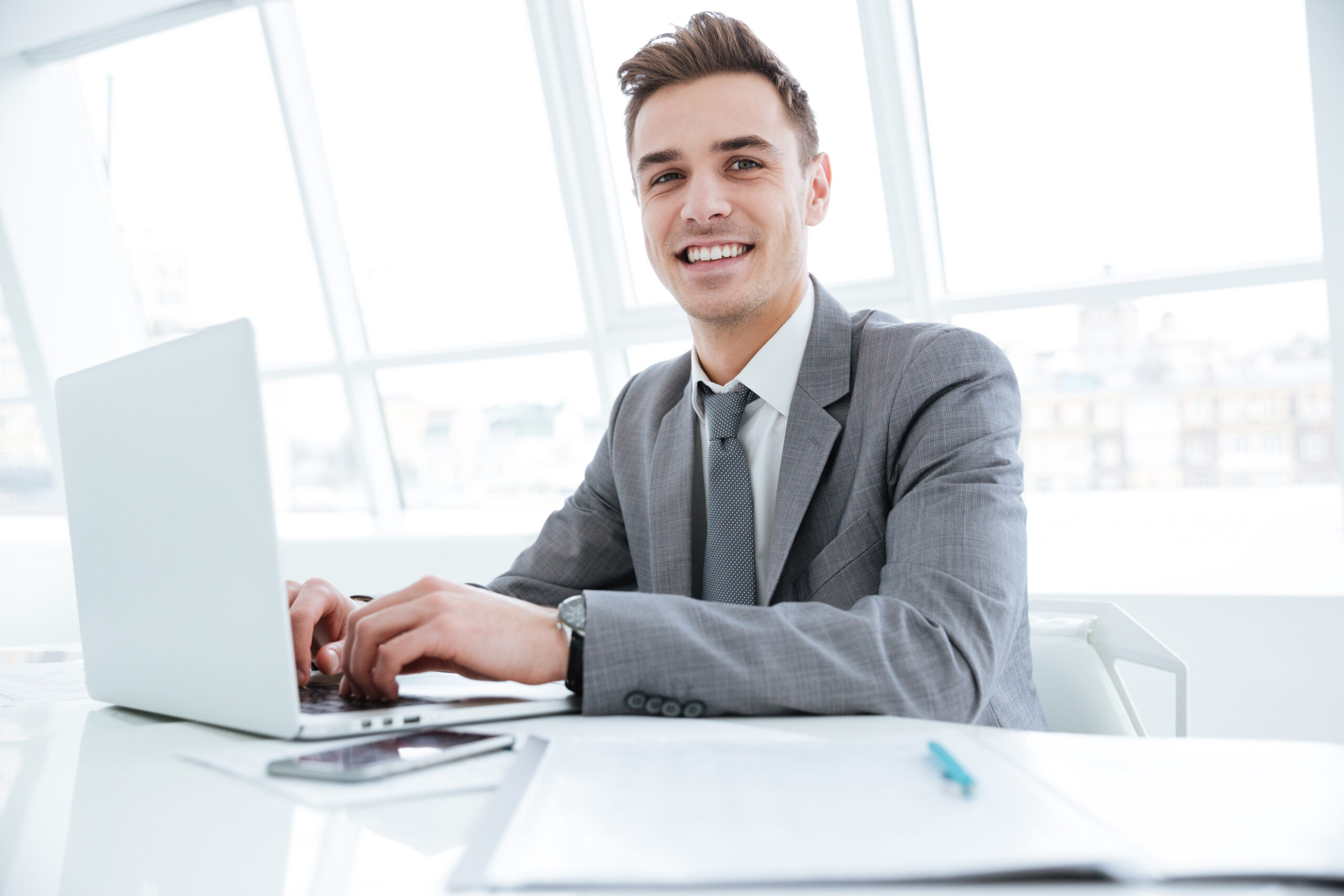 Smiling male marketing learner in business suit typing on laptop
