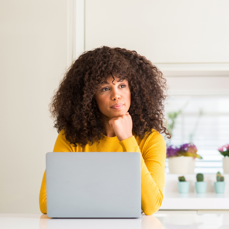 Woman sitting in front of laptop with her hand tucked under chin.