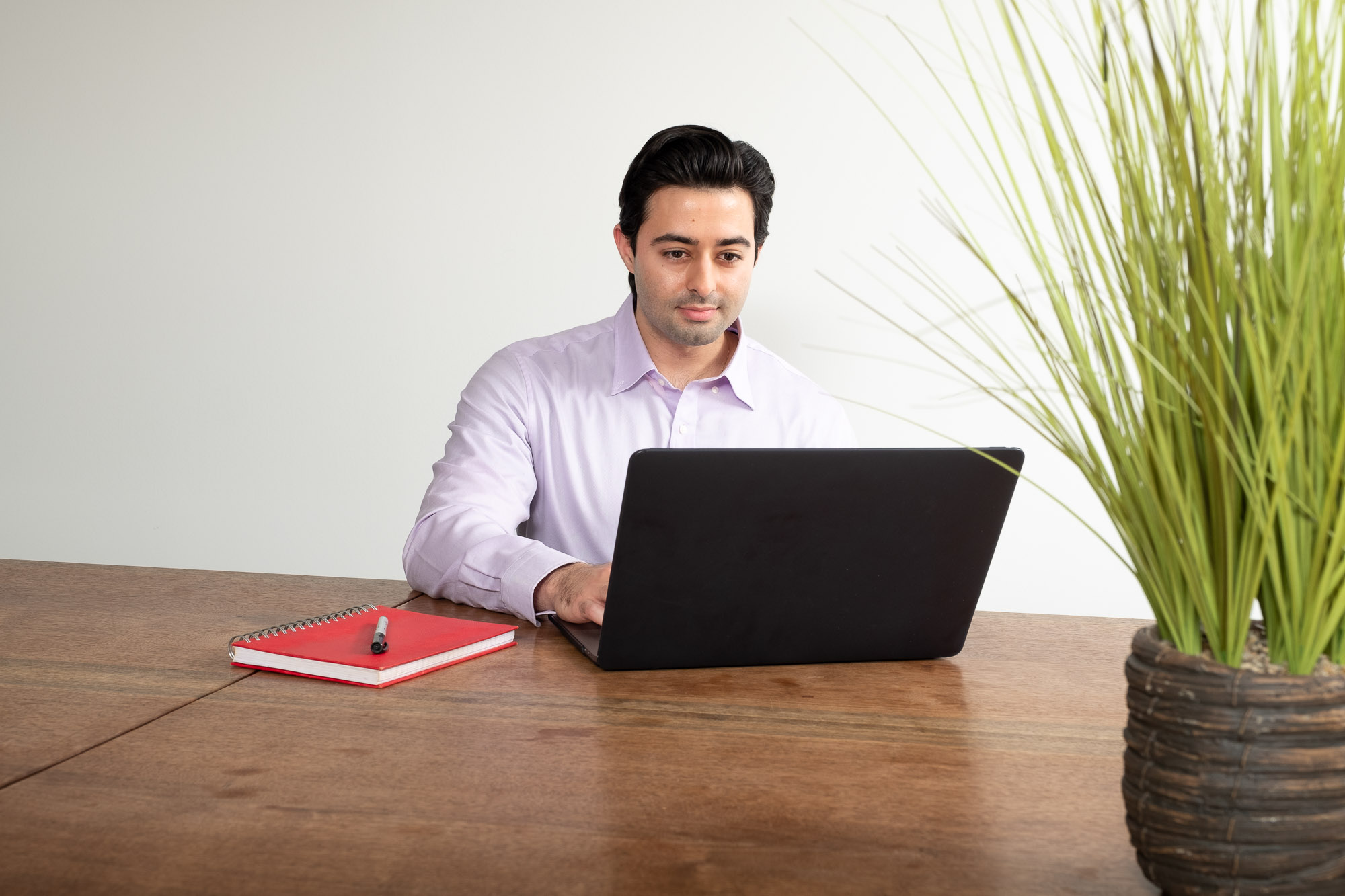 Fred seated at table with open laptop with a red notebook beside him. 