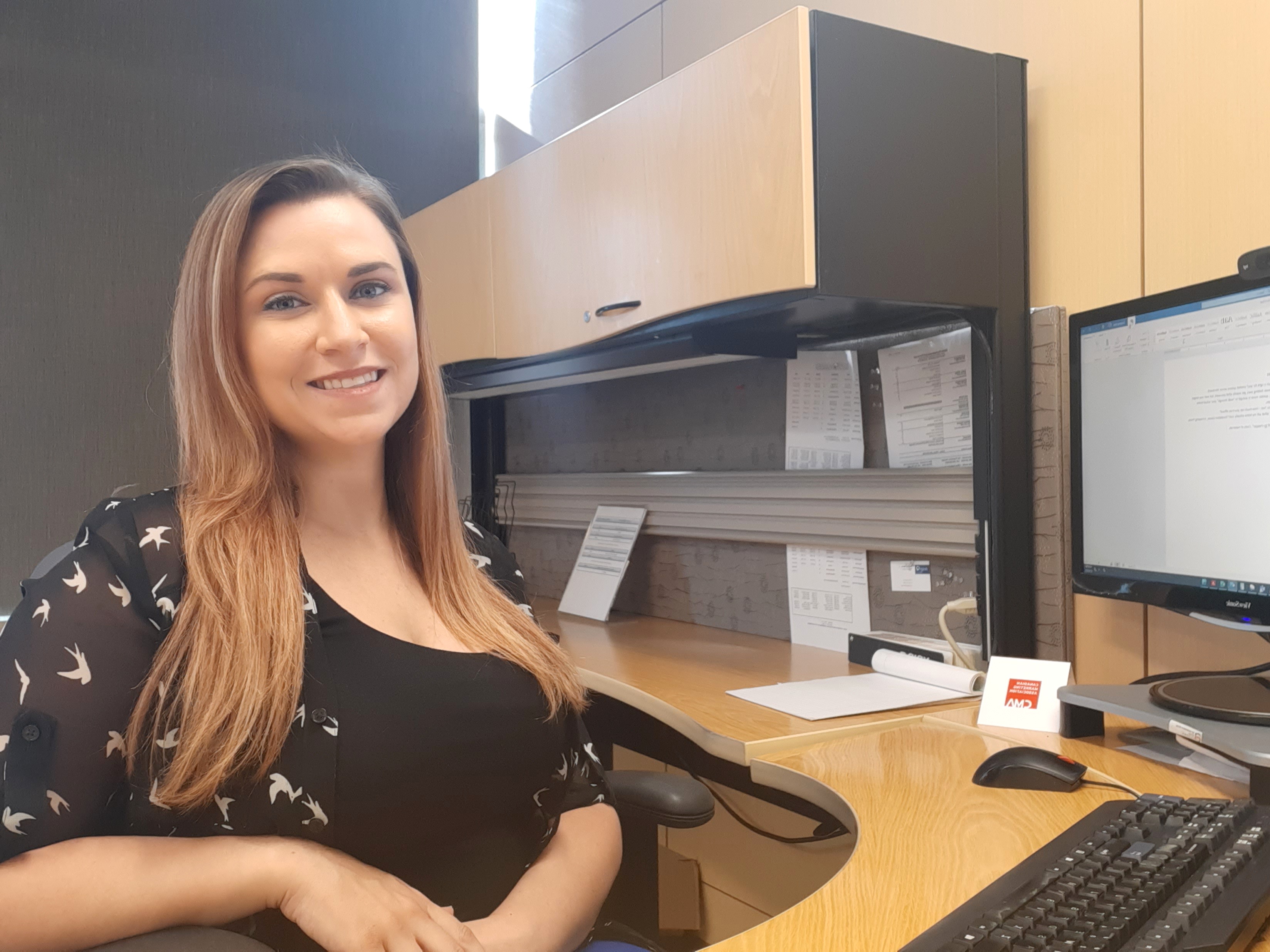 Courtney smiling and sitting at her desk in front of a computer. 