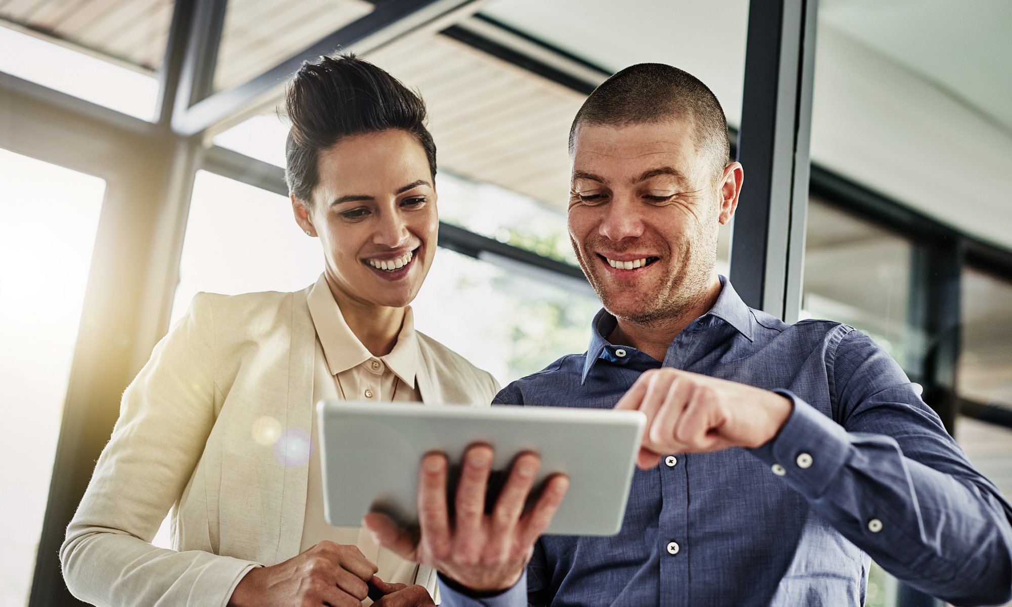 Two professionals smiling and staring at a smart tablet in office. 