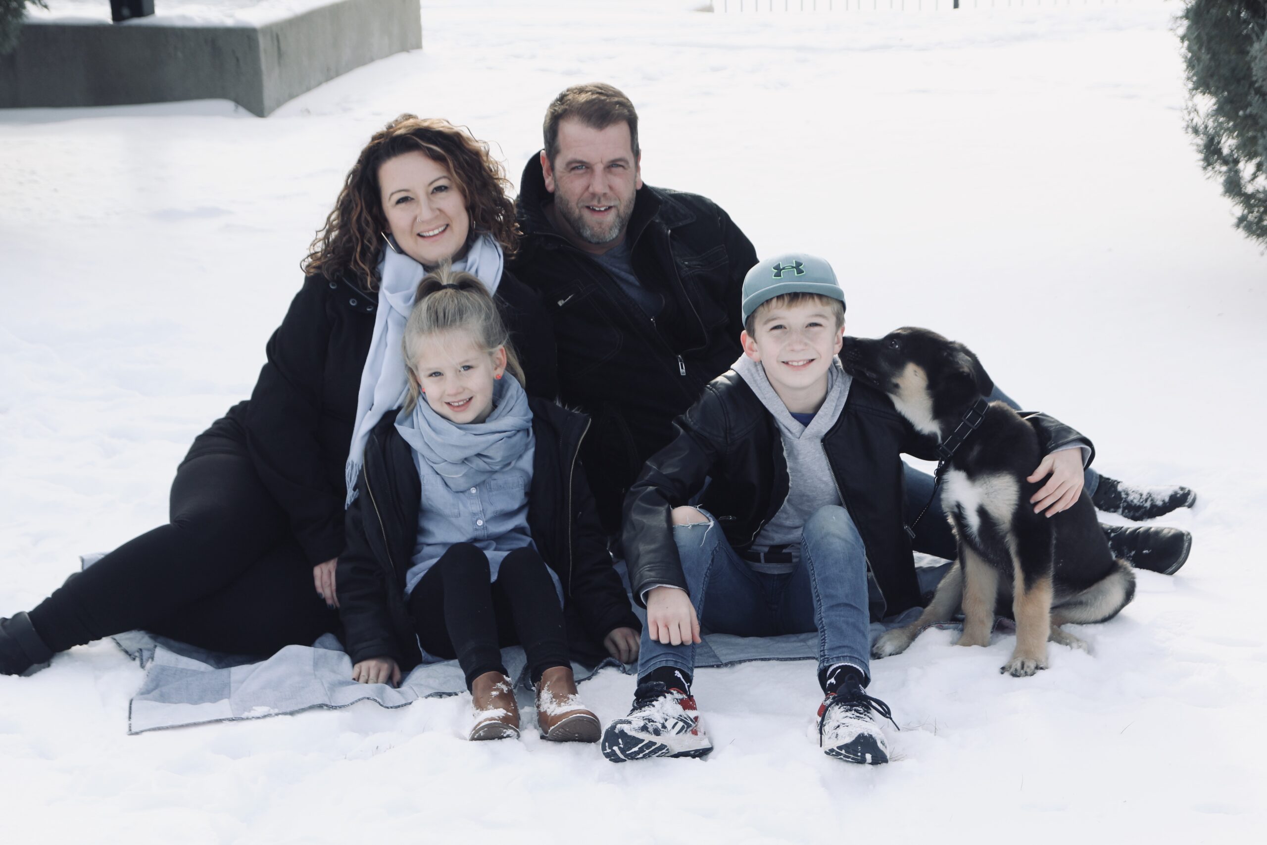 Aftan Chobot, CM, smiling with her family and pet dog outside in the snow. 