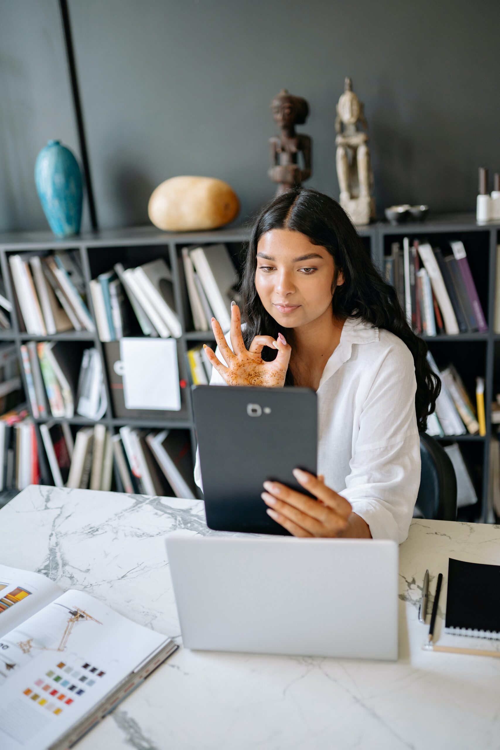 Calm professional signaling "OK" sign while on video call at her desk. 